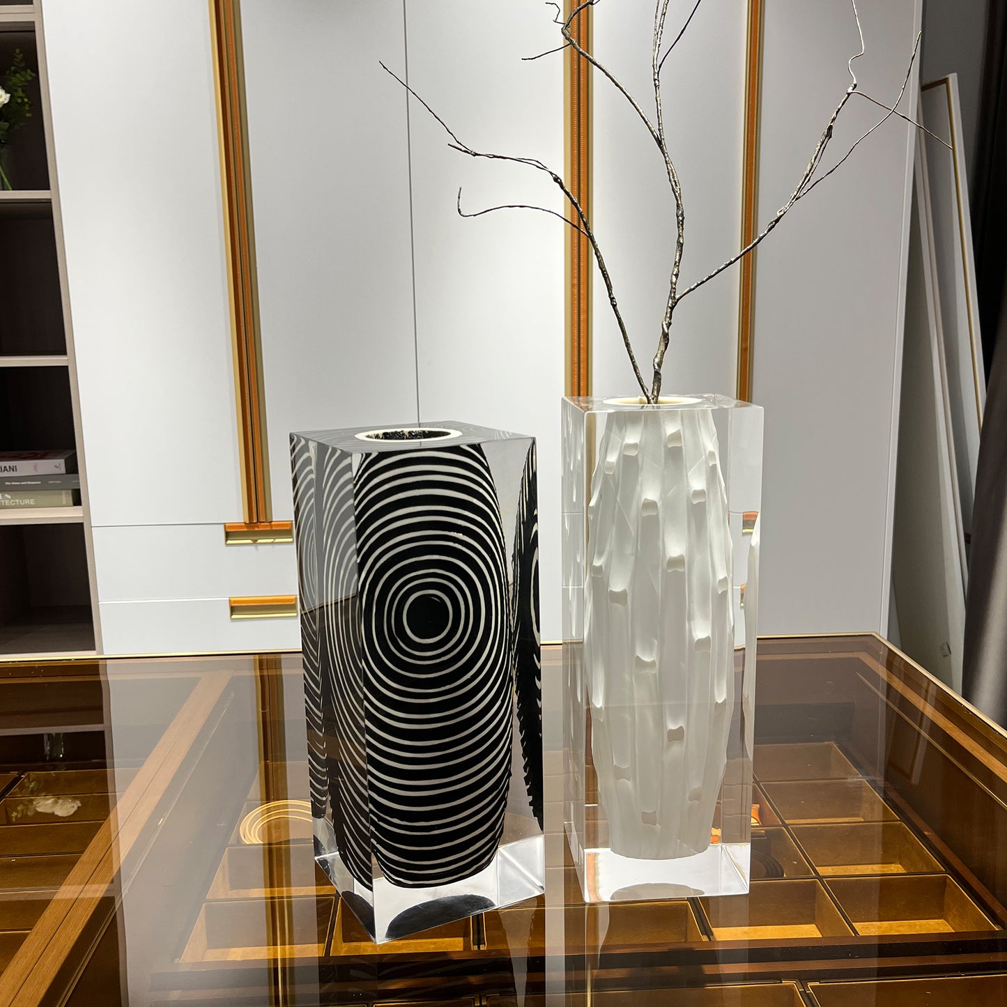 White striped vase encased in acrylic displayed next to a black spiral-pattern vase on a glossy tabletop. Contemporary art vases with a glass exterior in a cloakroom for luxury home decor.