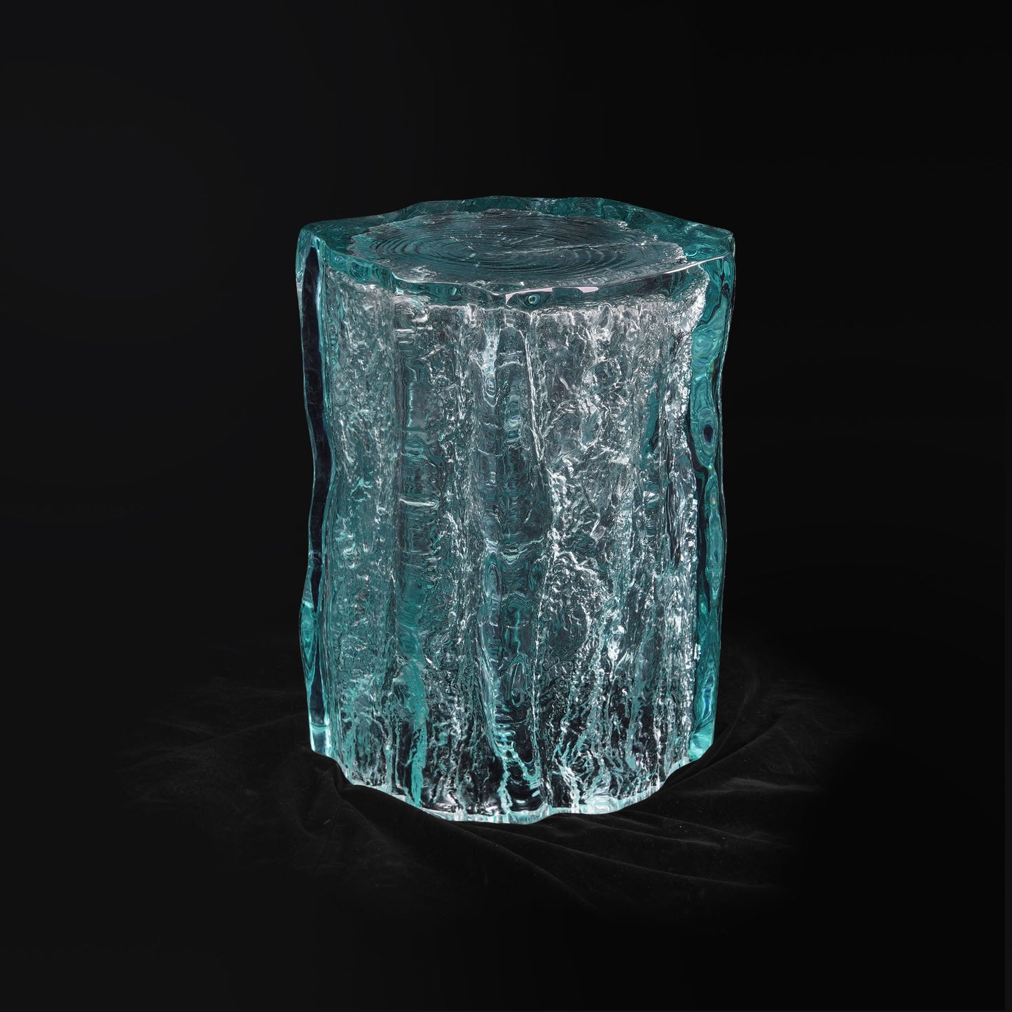 Tempered glass liked side table with rustic texture inside abstract irregular column shape. Entryway stool with a clear look siting in a black space.